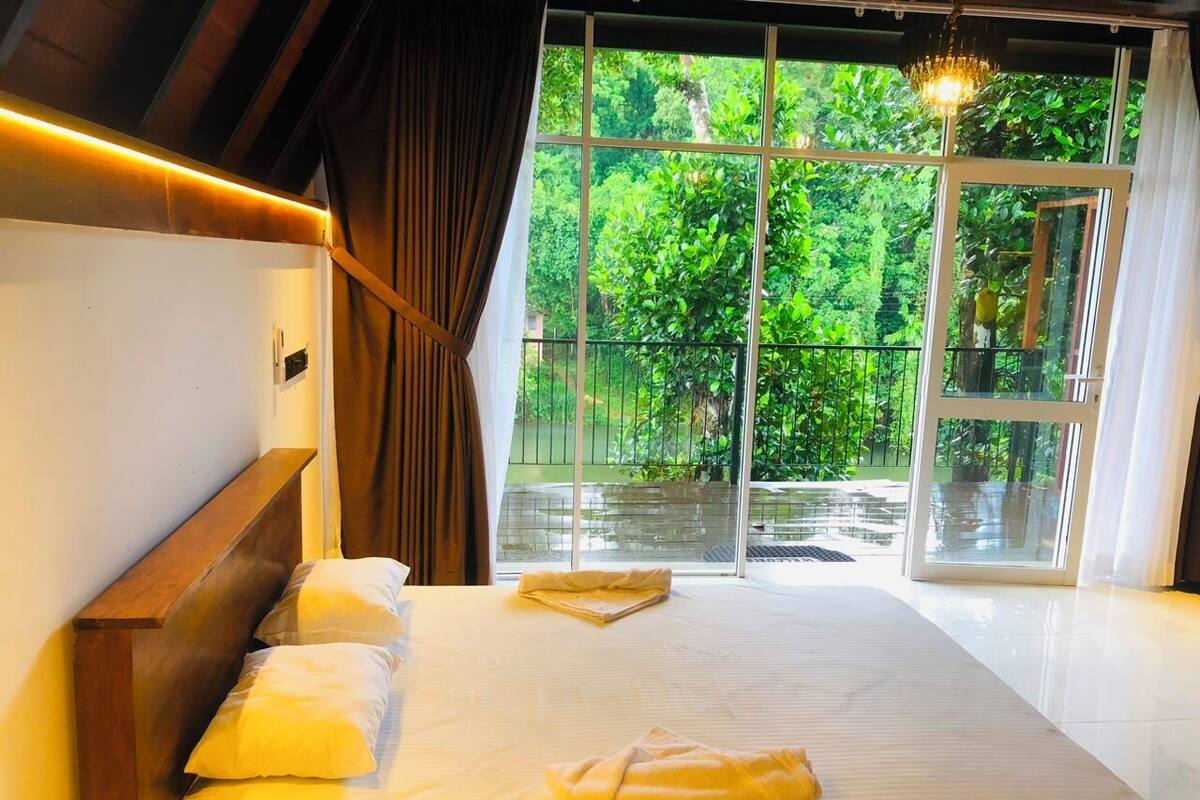Une chambre à coucher avec un grand lit, une tête de lit en bois, une fenêtre donnant sur un paysage verdoyant et un lustre.