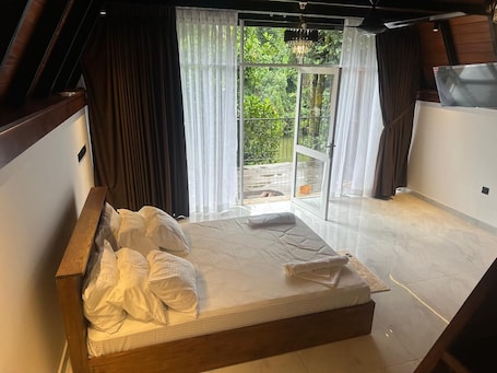 A bedroom with a bed, a view of greenery outside, and a sliding glass door.. Kithulgala Cabana Resort