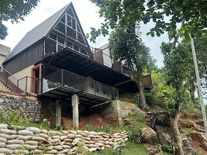 A modern house with a sloped roof, a balcony, and a stone foundation. - Kithulgala Cabana Resort (Kithulgala)