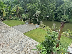 A stone-paved area with a grassy lawn and a body of water, surrounded by dense greenery. - Kithulgala Cabana Resort (Kithulgala)