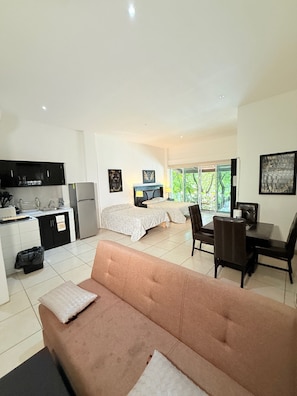 A modern living room with a sofa, a dining table, a kitchen area, and a bedroom with two beds. - CONDO W/ BALCONY JUST STEPS FROM BEACH N BOARDWALK (Puerto Vallarta)