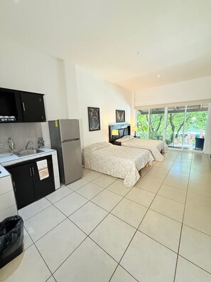 A room with a kitchenette, two beds, a TV, and a view of greenery outside. - CONDO W/ BALCONY JUST STEPS FROM BEACH N BOARDWALK (Puerto Vallarta)