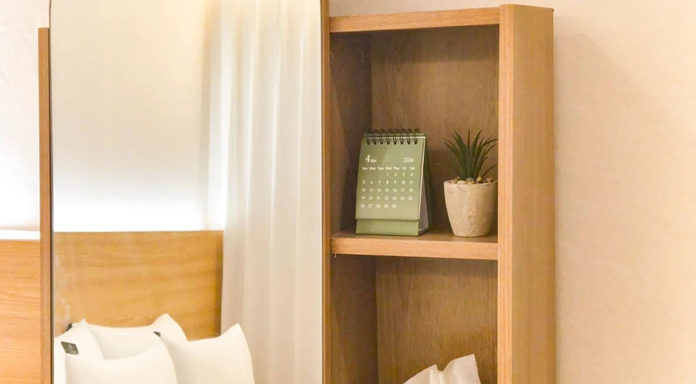 Una estantería de madera con un calendario verde, una planta en maceta y almohadillas blancas.