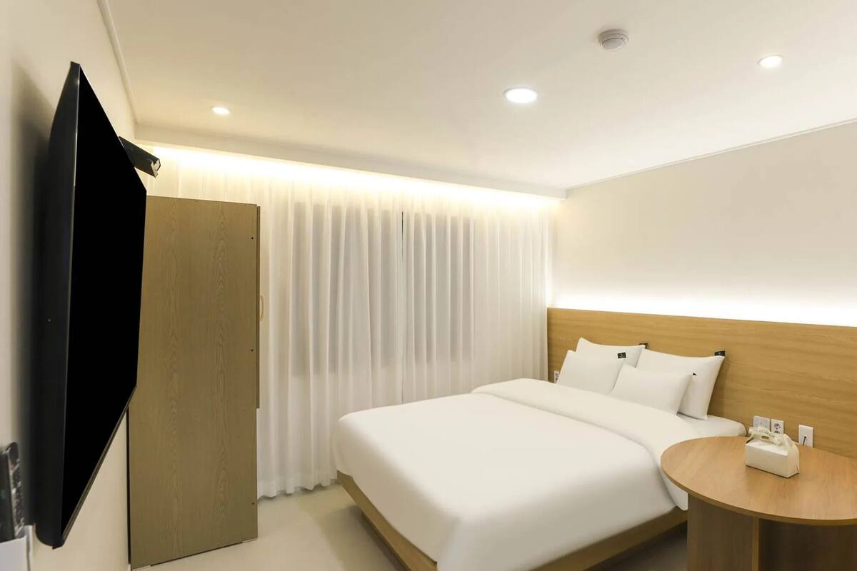 A hotel room with a bed, a bedside table, a TV, and a window with curtains.
