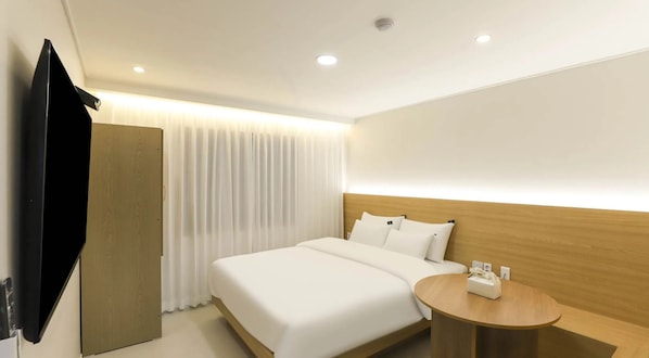 Habitación de hotel con cama, mesita de noche, televisión y ventana con cortinas.