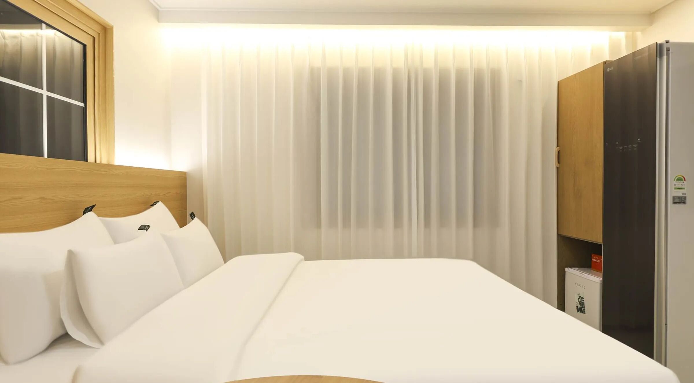 Une chambre d’hôtel avec un lit, une tête de lit en bois, une armoire et une fenêtre avec des rideaux.