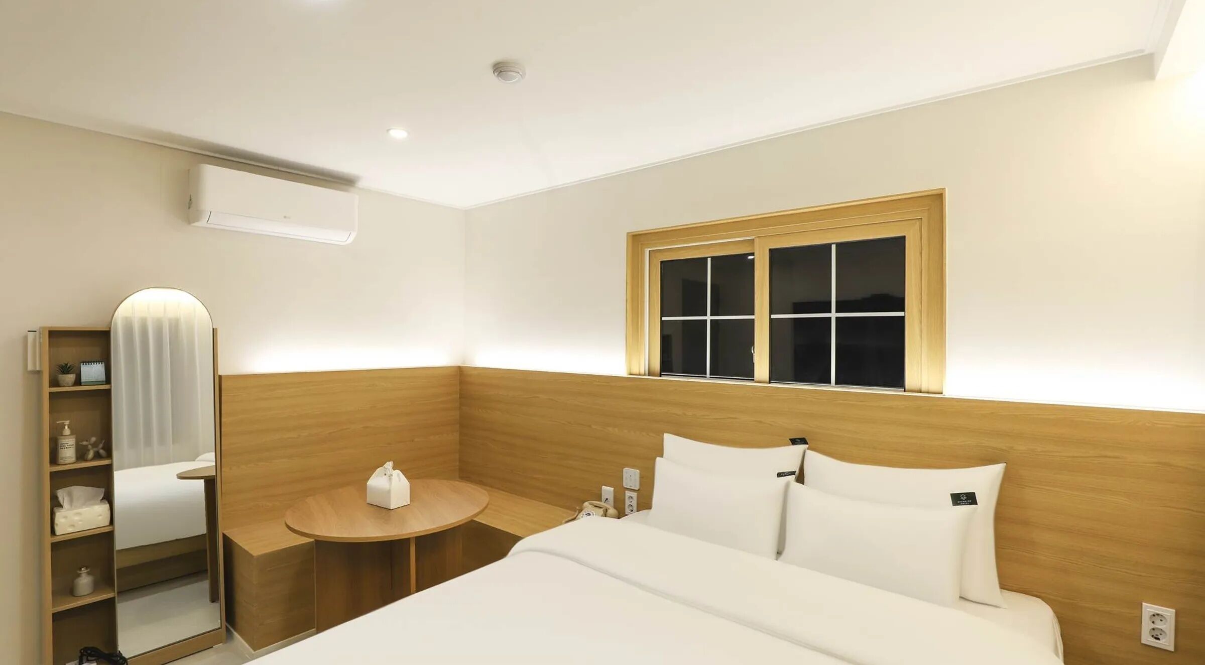 Habitación de hotel con cama, mesita de noche, espejo y ventana con persianas.