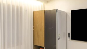 A room with a wooden wardrobe, a white wall, and a black screen mounted on the wall. - Hotel GEUMO on (Gumi)