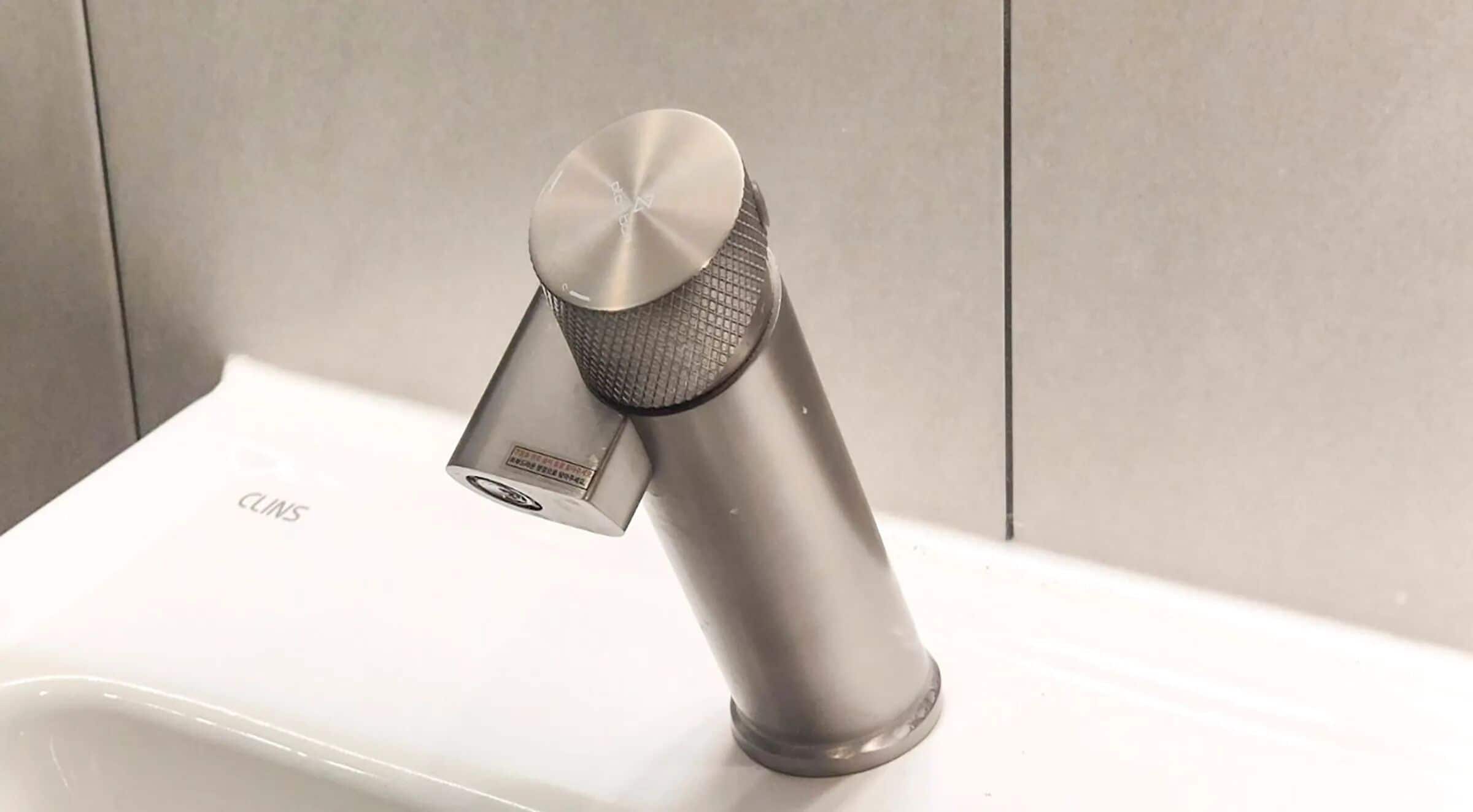 Un robinet moderne au fini métallique, doté d’une poignée circulaire au design original, installé sur un comptoir blanc.