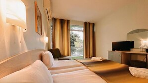 A hotel room with two beds, a desk with a television, a chair, and a window with curtains.