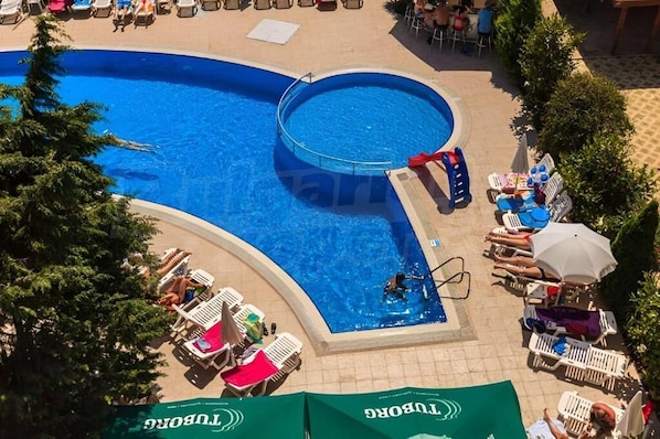 Ein Schwimmbecken mit Liegestühlen und Sonnenschirmen, umgeben von viel Grün.