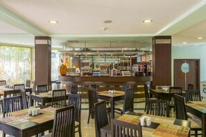 Un restaurante con mesas y sillas, una zona de bar con diversos elementos, y vistas al exterior.