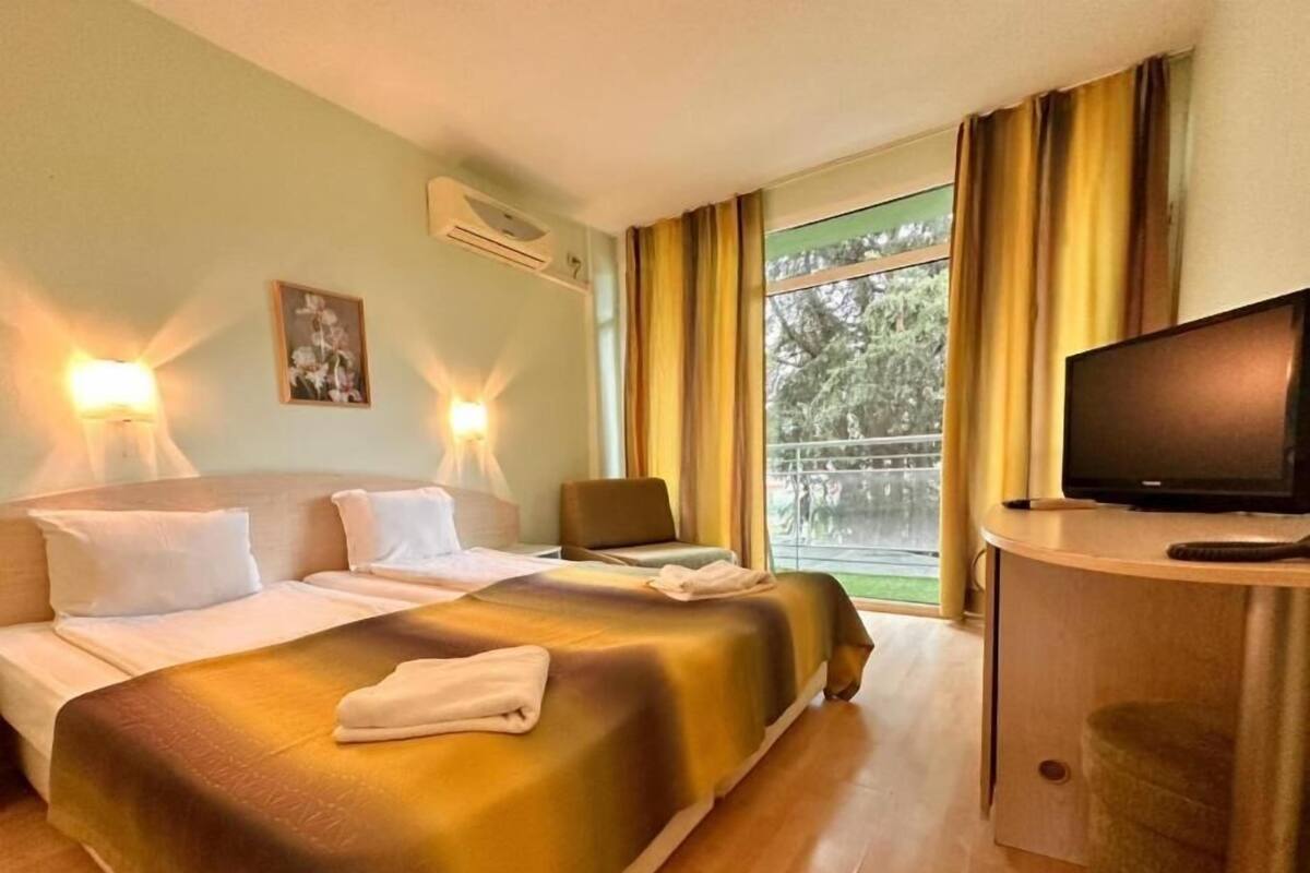 A hotel room with a bed, a desk with a television, and a window with curtains.