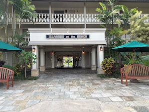 Entrada de un hotel con un letrero que dice 'Island on the Beach', paseo empedrado de piedra, bancos de madera y plantas tropicales.
