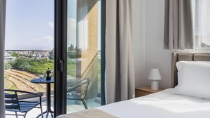 Hotellihuone, jossa on sänky, pöytä ja tuoli, lamppu sekä suuri ikkuna, josta avautuu näkymä kaupungin ylle.