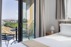 Une chambre d’hôtel avec un lit, une table et une chaise, une lampe, et une vue sur le paysage urbain par une grande fenêtre.