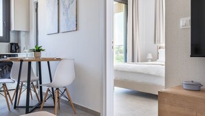 Moderni hotellihuone, jossa on sänky, yöpöytä, pieni keittotila ja ruokapöytä tuoleineen.