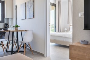 A modern hotel room with a bed, a bedside table, a small kitchen area, and a dining table with chairs. - Park View Retreat Limassol Pool & Free Parking (Limassol)