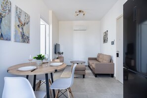 A modern living space with a dining area, sofa, TV, and a black refrigerator. - Park View Retreat Limassol Pool & Free Parking (Limassol)