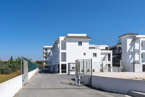 Un immeuble résidentiel moderne doté d’une entrée sécurisée, de nombreux balcons et offrant une vue sur un ciel dégagé.