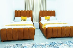 Twee bedden met bruine hoofdeinden, wit beddengoed en gele accenten.