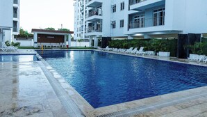 Una piscina con sillas de descanso, un edificio con la leyenda 'LOUNGE' y una estructura residencial de varios pisos.