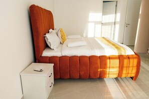 Un lit au design original, une table de chevet avec une télécommande et une porte visible au fond.