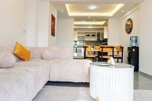 A modern living room with a sofa, a coffee table, and a dining area with chairs. - 2Bedroom Mombasa Nyali near the beach/AC/swimming pool/Netflix (Mombasa)