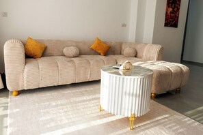 Ein beiges Sofa mit zwei runden Kissen und einem weißen Beistelltisch mit goldfarbenen Beinen.