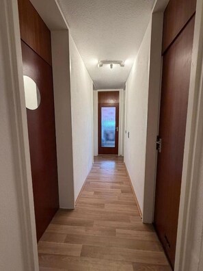 Un couloir étroit aux murs et au plancher en bois, qui mène à une porte dotée d’un panneau en verre dépoli.