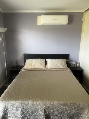 Ein Schlafzimmer mit einem Bett, zwei Nachttischen, einer Lampe und einer Klimaanlage an der Wand.