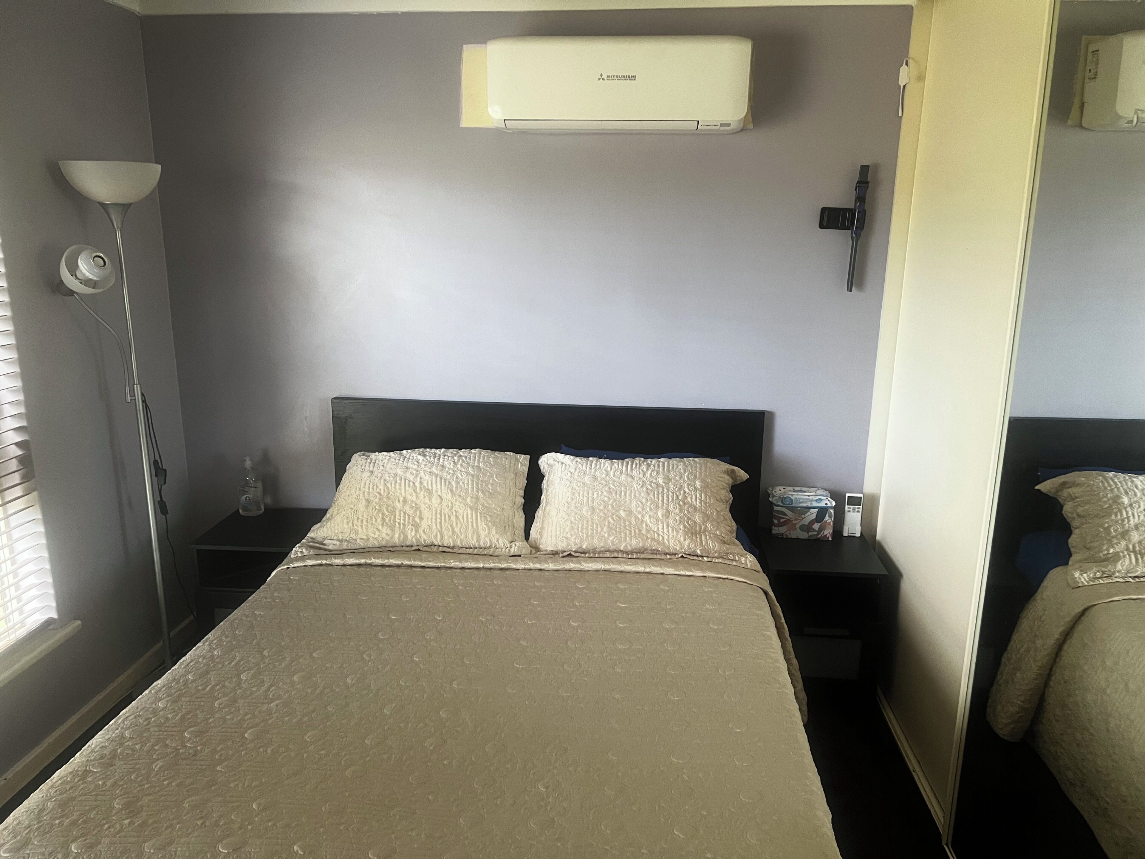 A bedroom with a bed, nightstands, a lamp, an air conditioner, and a mirror.. Cheap Room in Parafield Gardens
