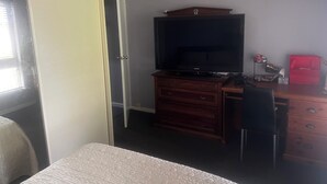 A hotel room with a bed, a TV on a wooden dresser, a desk with a chair, and a wardrobe. - Cheap Room in Parafield Gardens (Parafield Gardens)