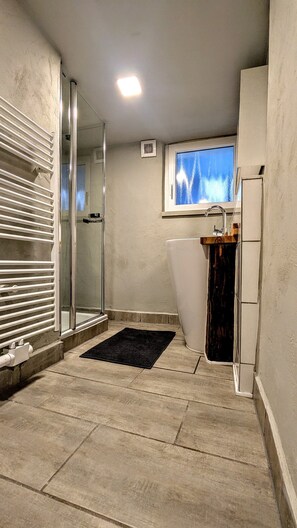 Une salle de bain avec une porte de douche en verre, un tapis noir, une fenêtre avec vue et un lavabo doté d’un plan de travail en bois.
