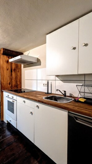 Une cuisine avec des armoires blanches, un plan de travail en bois, un four encastré, un évier et un lave-vaisselle.