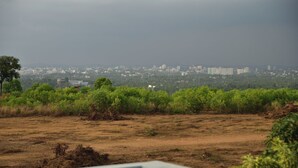 A view of a cityscape with buildings in the distance, a grassy area in the foreground, and a cloudy sky.