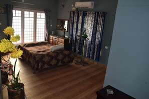 A bedroom with a bed, dresser, mirror, potted plants, and a window with curtains.