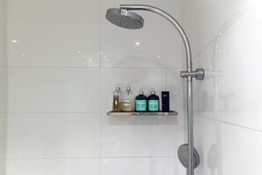 A shower with a handheld showerhead, a wall-mounted control, and a shelf with toiletries. - Modern Town House (East Fremantle)