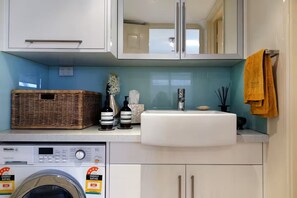 A modern kitchen with a washing machine, a sink, and a basket on the countertop. - Modern Town House (East Fremantle)