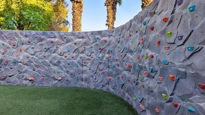 Un mur d’escalade avec des prises de différentes couleurs et une zone herbeuse à sa base.
