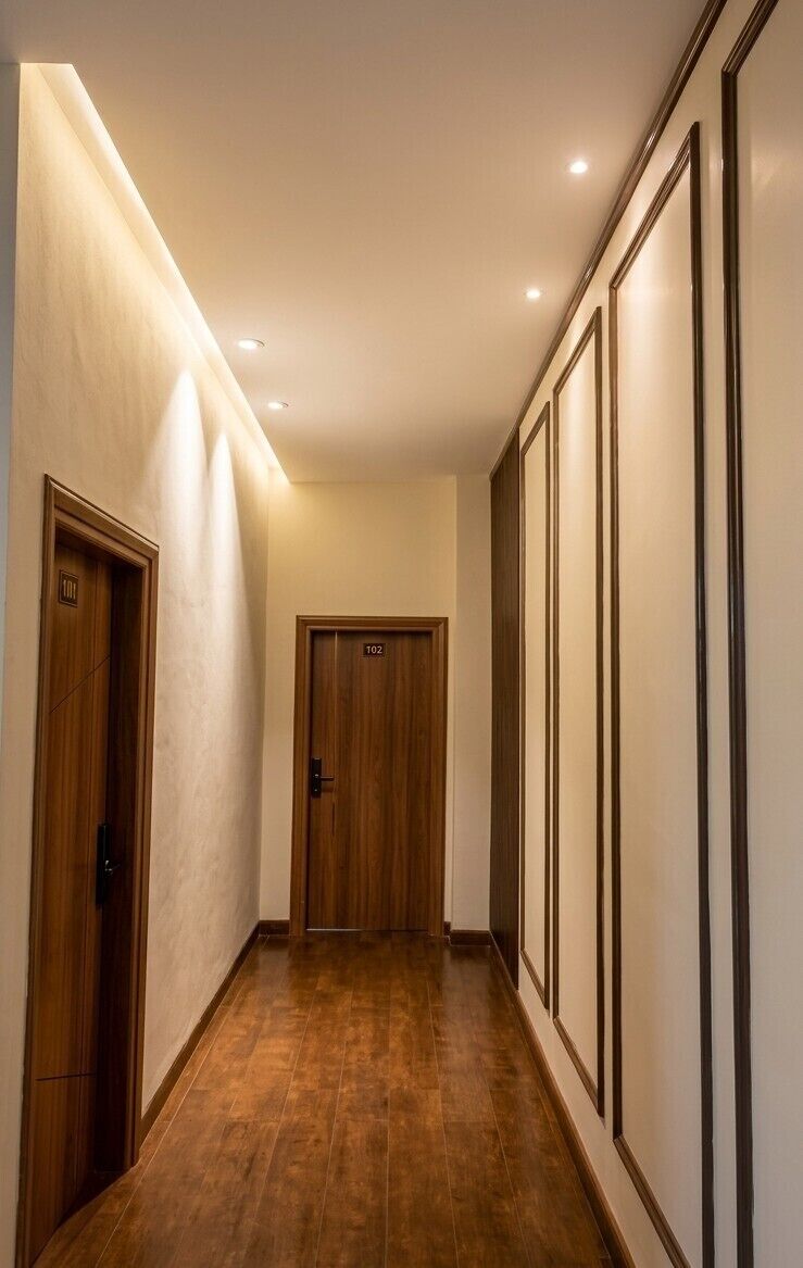 Un pasillo con puertas de madera, luces empotradas y suelo de baldosas.