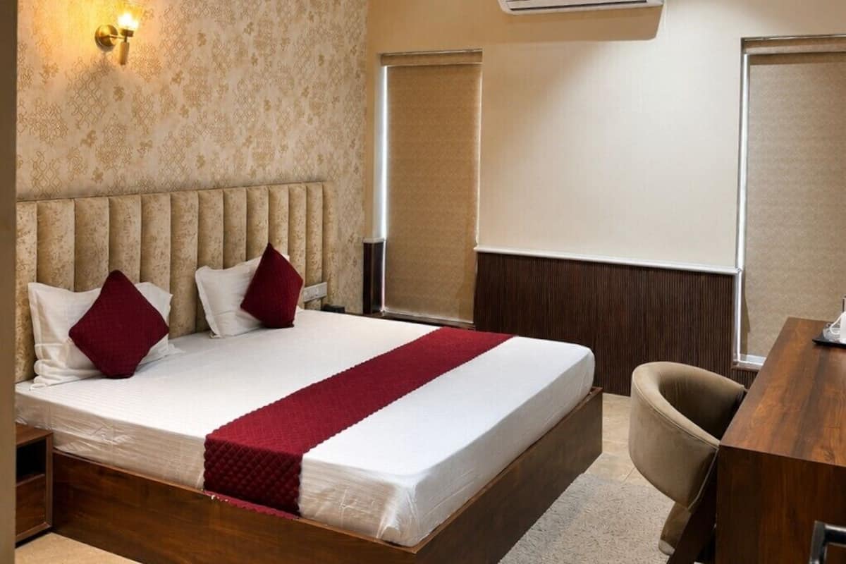 Una habitación de hotel con cama, escritorio, aire acondicionado, ventilador de techo y lámpara de pared.