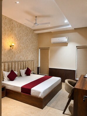 Une chambre d’hôtel équipée d’un lit, d’un bureau, d’un climatiseur, d’un ventilateur de plafond et d’une lampe fixée au mur.
