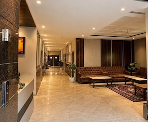 A hotel lobby with a reception desk, a brown leather sofa, a coffee table, and potted plants. - GRAND VISTA SANGRUR (Sangrur)