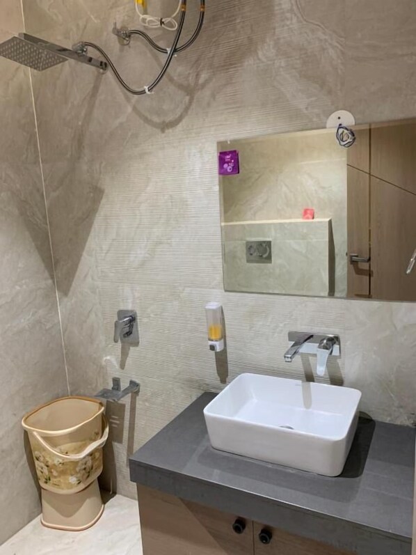 A bathroom with a rectangular sink, a mirror, a showerhead, and a trash bin. - GRAND VISTA SANGRUR (Sangrur)