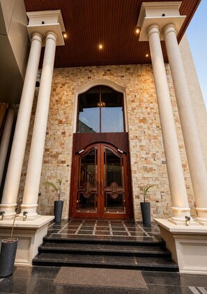 Une entrée d’immeuble avec une façade en pierre, de grandes colonnes et une porte en bois.