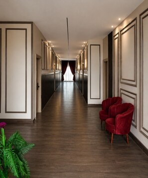 A hotel hallway with a long corridor, doors on both sides, and a red chair in the foreground. - GRAND VISTA SANGRUR (Sangrur)