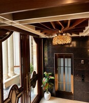 Un vestíbulo con techo de madera, una lámpara moderna, una planta en maceta y una puerta con panel de vidrio esmerilado.