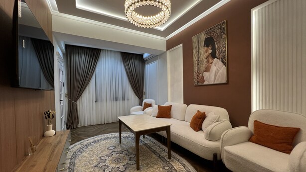 A modern living room with a sofa set, a coffee table, a patterned rug, a chandelier, and a painting on the wall.