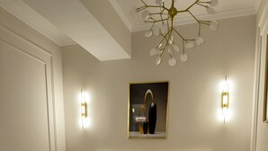 A bedroom with a large bed, two bedside tables, a nightstand, a chandelier, and a framed artwork on the wall.